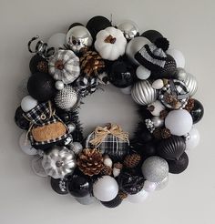 a wreath made out of black, white and silver christmas ornaments is hanging on the wall