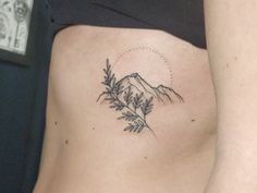 a woman's lower back tattoo with mountains and leaves on her side ribcage