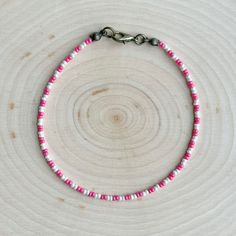 a pink and white beaded necklace on a wooden surface with a metal clasp in the middle