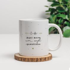 a white coffee mug sitting on top of a wooden coaster next to a potted plant