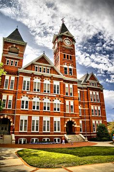 an old brick building with two towers and a clock on the top, under a cloudy sky