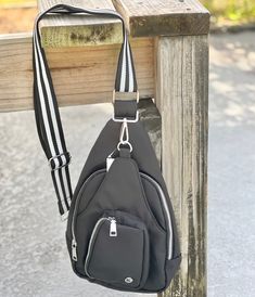 a black purse hanging from a wooden rail on the side of a bench with a striped strap around it