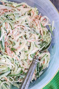 a bowl filled with pasta and vegetables on top of a green table cloth next to a spoon