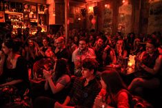 a large group of people sitting in a room with candles on the floor and one person standing up