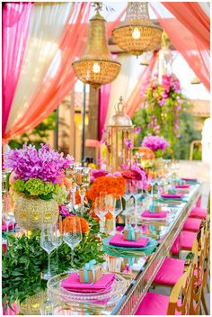 a table set up for a party with pink and orange flowers on the table cloth