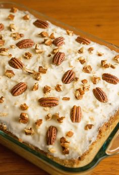 a cake with white frosting and pecans on top sitting on a wooden table