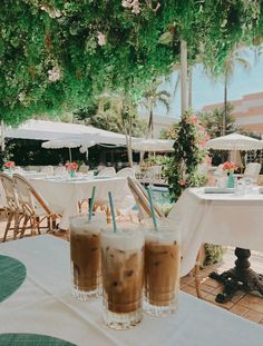 two drinks sitting on top of a table next to an umbrella covered area with tables and chairs