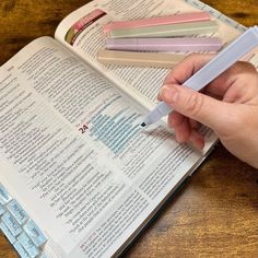 a person is holding a pen over an open book on a wooden table with keyboard keys