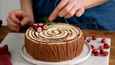 a person decorating a cake with icing and cranberries on a table