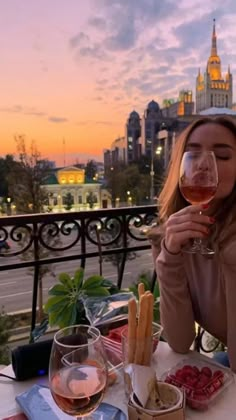 a woman sitting at an outdoor table drinking wine