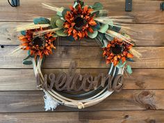 a wreath with sunflowers and the word welcome hanging on a wooden wall behind it