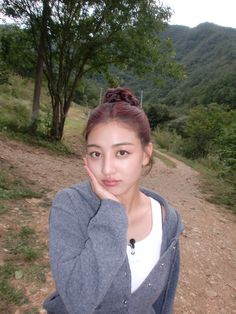 a woman standing on a dirt road with her hand to her face and trees in the background