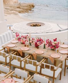 a table set up with pink flowers and place settings in front of an ocean view