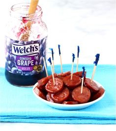 a bowl filled with hot dogs and toothpicks next to a jar of grapes