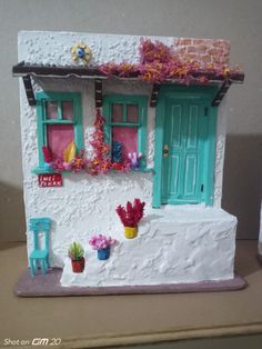 a doll house with flowers and potted plants on the front porch, next to a brick wall