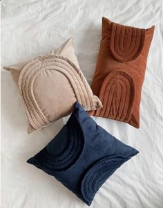 three pillows on a bed with white sheets and brown, blue, and tan colors