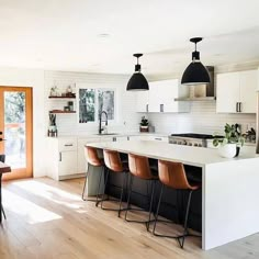 a kitchen with an island and bar stools next to the counter top, along with white cabinets and black pendant lights