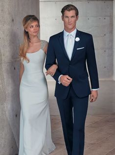 a man in a suit and woman in a white dress walking down a hall together