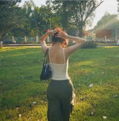 a woman standing in the grass with her back to the camera and holding a handbag