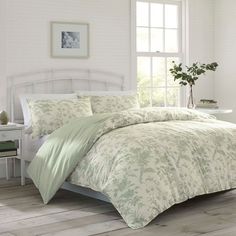 a white bed with green comforter and pillows in a room next to a window