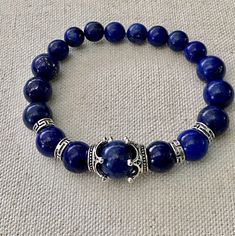 Beautiful natural  Dark Blue Lapis Lazuli gemstone beads. The center bead is 12mm and on each side 10mm beads and goes down to 8mm beads. Crown bead caps surround the focal bead.  A beautiful natural Lapis Lazuli stretch bracelet. Great by itself or stacked.  The black and white Krobo bead bracelet in the last pictures is sold separately in another listing here in my Etsy Shop. Spiritual Lapis Lazuli Round Beads Bracelets, Lapis Lazuli Gemstone Beaded Bracelets, Lapis Lazuli Beaded Bracelets With Gemstone, Lapis Lazuli Beaded Bracelets With Polished Round Beads, Adjustable Lapis Lazuli Stretch Bracelet With Round Beads, Hand-strung Lapis Lazuli Beaded Bracelets, Beads Crown, Lapis Lazuli Gemstone, Lapis Lazuli Beads