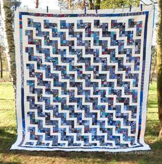 a blue and white quilt hanging from a tree in the grass with trees behind it