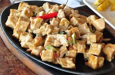 tofu and vegetables on a black plate with chopsticks in the foreground