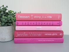 a stack of pink books sitting next to a potted plant