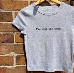 ✿ I'm with the band embroidered baby tee 🎸 - ✿ 'I'm with the band' slogan in black thread, embroidered on a grey cropped baby t-shirt! Perfect for going to see your favourite band live  - ✿ Micro-rib material, so it's super soft and comfy!  - ✿ Please look at the last slide for the size guide! I do not accept returns if you pick the wrong size, so please make sure you choose the correct one! They are designed to fit close like a baby tee - ✿ I have lots of other items on my page! This would be Fitted Gray Cotton T-shirt, Fitted Crew Neck Tops With Embroidered Text, Fitted Cotton T-shirt With Band Logo, Gray Cotton Band Merch Tops, Cotton Crew Neck Top With Band Logo, Fitted T-shirt With Embroidered Text And Short Sleeve, Unisex Short Sleeve Tops With Band Logo, Unisex Cotton T-shirt With Band Logo, Fitted Cotton T-shirt With Band Merch