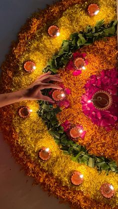 a person reaching for candles on top of a flowered circular arrangement with flowers and leaves