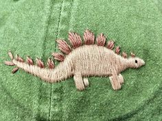 a close up of a dinosaur embroidered on a green hat