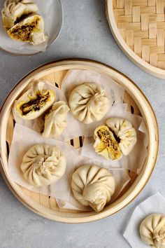 several small dumplings are placed in a bamboo tray on a gray surface next to plates and bowls