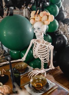 a skeleton sitting on a table in front of some balloons and other decorations with candles