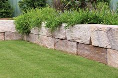 a stone wall with grass and bushes in the background