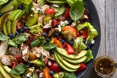 a salad with chicken, avocado, strawberries and blueberries