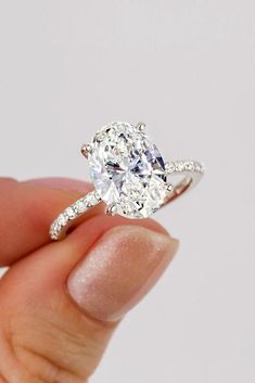 a person holding an oval diamond ring in their left hand, with the center stone surrounded by small diamonds