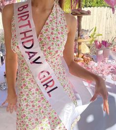 a woman wearing a pink flowered dress with a sash around her neck and the words birthday girl on it