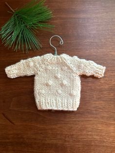 a knitted sweater hanging from a hook on a wooden table next to a pine tree