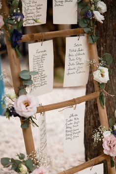 a wooden ladder with seating cards attached to it and flowers on the sides, along with greenery