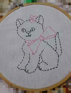 a white cat with a pink bow on it's head is sitting in front of a cross - stitch pattern