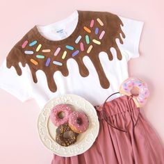 a white shirt with chocolate frosting and donuts next to a pink skirt on a pink background