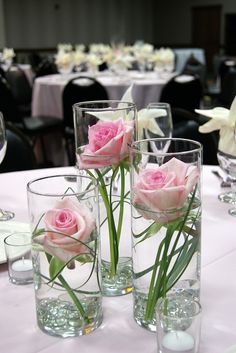 three vases filled with pink roses sitting on top of a white table cloth covered table