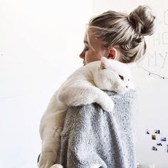 a woman holding a white cat wrapped in a gray sweater and looking at the camera