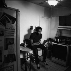 a black and white photo of a man sitting at a table in a kitchen with his feet on the counter