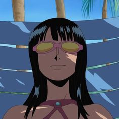 a woman with long black hair and sunglasses on her face, standing in front of palm trees