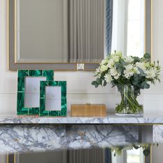 a marble table topped with a vase filled with flowers next to a mirror and photo frame