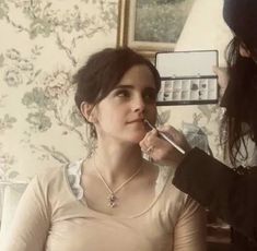 a woman is getting her makeup done while another person looks in the mirror behind her