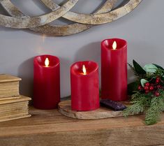 three red candles sitting on top of a wooden table next to a pile of books