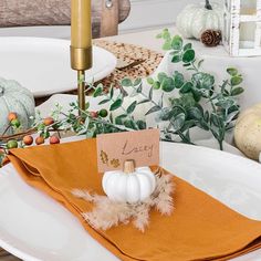 a place setting with white pumpkins and greenery