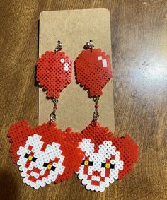 two red heart shaped earrings on top of a wooden table